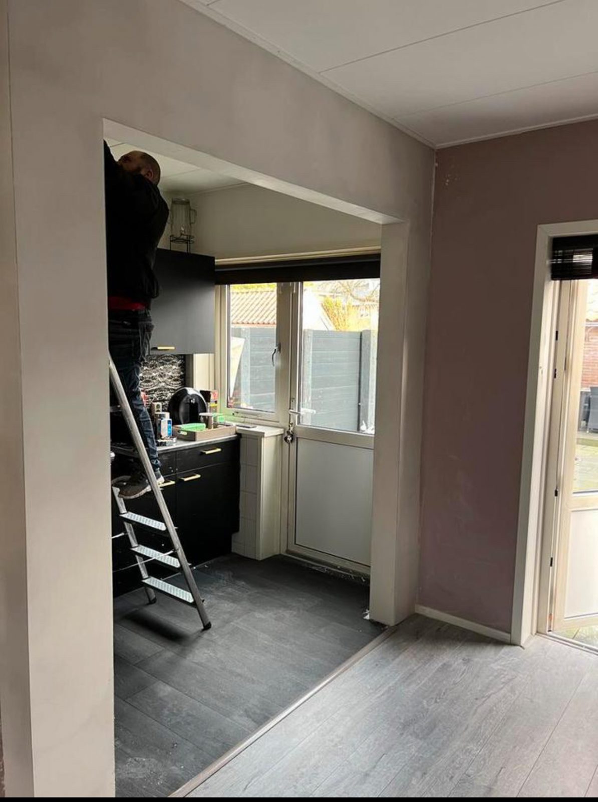 Vakman van Klusbedrijf Oranje stuukt een keuken en doorgang vanaf de ladder